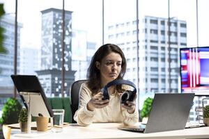 Joyful female CEO working on her business and listening to audiobook, using headset and multitasking in smart urban office. Confident entrepreneur having fun with interesting podcasts, office life. photo