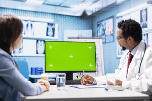 African american medic points at green screen on computer while he consults his patient, exploring treatment plans on health insurance. Physician gives medical advice to ill woman. photo