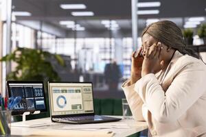 Stressed company CEO rubbing head temples while checking performance targets for revenue, unhappy with figures. Exhausted woman suffering painful migraine while reviewing administrative policies photo