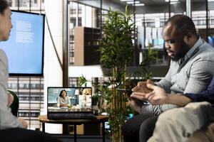 African american man doing videocall with colleagues in company office. Worker talking over remote videoconference meeting with business partners inquiring about commissioned project progress photo