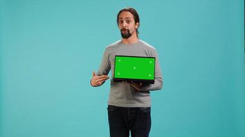 Tech content creator doing influencer marketing using green screen laptop, isolated over studio background. Arab man holding empty copy space mockup notebook, doing review, camera A photo