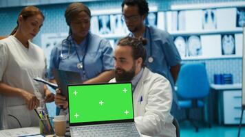 Diverse team of specialists examining radiography test scans with isolated screen in a meeting, reviewing x ray results at a treatment center. Staff ensuring disease prevention. Camera B. photo