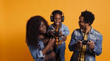 Joyful optimistic dad playing online games with his boy using controller, parents enjoying leisure time with their small child. African american happy family play together in studio. Camera B. photo