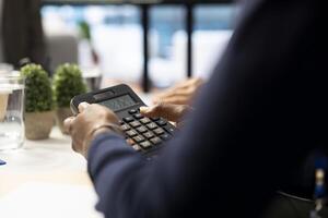 Accountant expert doing finances and calculating the budget using a calculator, discussing about resources allocation in a corporation meeting. Multinational company management. Close up. photo