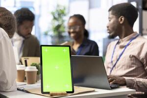 Marketing team reviews performance metrics next to green screen on tablet, leveraging big data insights and detailed analytics to refine strategies and enhance project effectiveness. photo