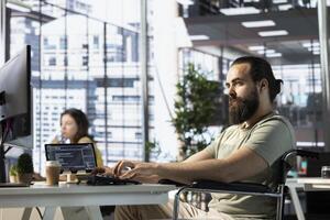 Developer with disability sitting in wheelchair fixing applications issues, dealing with databases and server configuration. Man with paraplegia optimizing company software for improved performance photo