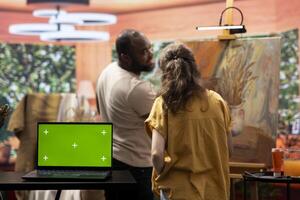 Diverse artists working on a new painting in workshop next to green screen, creating a rustic artwork on canvas with watercolor paint. Team of painters using a certain painting technique. photo