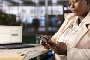 Accountant in modern startup agency using mobile phone to text friends after inputting financial figures on laptop. Close up of focused businesswoman typing on smartphone while working in office photo