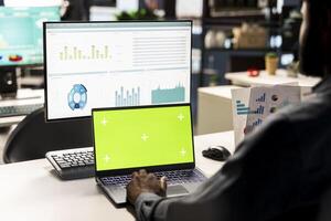 Black businessman analyzing financial data next to chroma key screen, reviewing company strategies on computer and contributing to business development and decision making. Successful forecast. photo