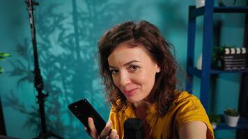 Reviewer discussing with viewers about newly released cellphone, capturing footage with handheld camera. POV of woman chatting with subscribers during stream, filming latest generation phone review photo