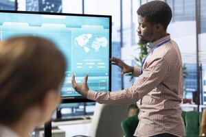 General manager making a presentation with infographics and sales numbers on interactive board, showing the organizational progress to the staff. Employees reviewing analytics plans. photo
