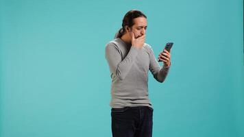 Man holding mobile phone, browsing betting website, celebrating after winning money, isolated over studio background. Cheerful person feeling happy while scrolling on smartphone, camera A photo
