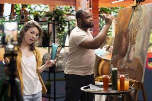 Artists recording the creative process of painting an artwork piece, hosting an online art class for instruction and remote learning. Diverse painters showing their supplies and paint tubes used. photo