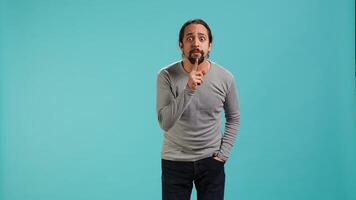 Portrait of man doing shushing hand gesturing, requesting silence. Person placing finger on lips, doing quiet sign gesture, asking for secrecy, isolated over studio background, camera A photo
