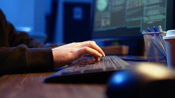 Hacker in secret underground shelter typing on keyboard, writing lines of code on computer, trying to get past security systems with virus. Scammer working on hacking script, camera A close up shot photo
