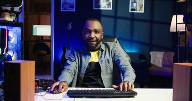 Joyous gamer competing in intense internet multiplayer videogame from vibrant living room with neon lights. Smiling african american man using PC, having immersive experience while gaming, camera B photo