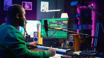 Songwriter taking notes to create new tracks for an album in his home studio, writing lyrics and harmonic elements before recording his song and editing on software, acoustical engineering. Camera B. photo
