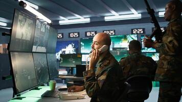Military officer in command post receiving telephone call while looking at intel files. Intelligence specialist reading opponents strategy mission case file and talking on phone, camera B photo