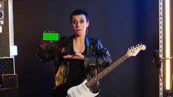 Cool rebellious rock star does a live performance pointing to copy space screen at nightclub, feeling powerful in her leather jacket and dark make up. Trendy powerful girl performing. Camera A. photo