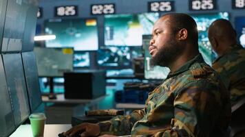 Military agent working overtime in control room to analyze aerial reconnaissance data, feeling tired. Exhausted intelligence corps agent controlling drones, suffering from headache, camera A photo
