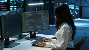 Engineer in data center sitting down at desk, installing software on computer, troubleshooting issues. Woman arriving at work in server hub, establishing performance benchmarks, camera A photo