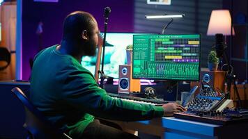 Sound engineer pressing keys of electronic synthesizer and composing new song, adjusting volume levels on pre amp knobs. Composer producing music on piano midi controller, mixing tunes. Camera A. photo