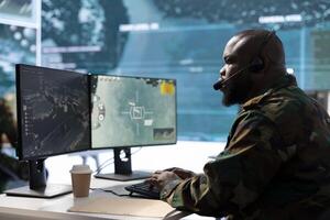 Military IT expert in a mission control center manages satellite data from cctv, communicating real time information for strategic operations in a command post base with high tech big screen. photo