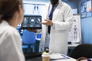 Physician presenting a ct scan result for heart and brain analytics during a meeting with medical staff, examining electrocardiogram tests on laptop. Licensed medics discuss recovery plan. photo