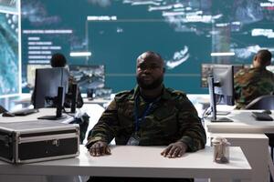 Military officer participates in a secure videoconference call in modern command center, transmitting live satellite information. Federal collaboration for national security operations. photo