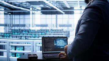 Software developer in data center using artificial intelligence computing simulating human brain. IT support staff member working on notebook with AI machine learning algorithms, camera B photo