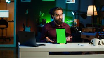 Tech specialist presenting chroma key tablet in entry level low budget price range to interested viewers, filming in studio. Viral content creator reviewing green screen digital device, camera A photo