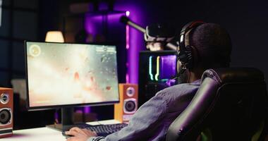 Pro gamer wearing headphones playing science fiction game. Content creator in gaming chair talking with audience on headset mic, filming tutorial on how to defeat enemies, camera B photo