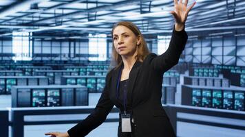 Software developer looking at holograms in data center, monitoring infrastructure. Woman in server room interacting with high tech augmented reality AI visualization, camera A photo