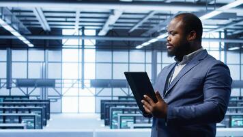 Software engineer in data center runs error checking utilities on tablet to fix problems. IT specialist looking for network issues affecting rigs performance using digital device, camera B photo