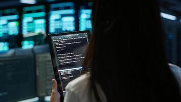 Data center software developer responsible for installation of networking equipment solving tasks on device. Close up of woman doing maintenance on server room infrastructure using tablet, camera A photo