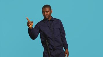 Portrait of security agent pointing finger at people, warning them while securing assigned post, studio background. African american guardian scolding trespassers, handling security breaches, camera B photo