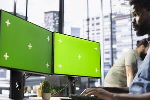 Company employee sitting at desk in office, doing research for team project on isolated screen PC. Man looking at chroma key computer monitor in workplace solving tasks during job shift photo