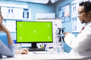 General practitioner consulting a female patient next to isolated chroma key display on pc, sharing insight on lab test results and analysis. Skilled medic supports his client, indoors check up photo