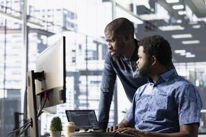 Data engineering IT staff members at PC desk developing machine learning algorithms. African american team in office solving tasks, training large scale deep learning models using computer photo