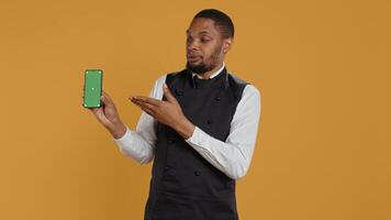 Restaurant staff showing a smartphone with green screen in studio, prepared to serve food orders in service oriented environment. Waiter with apron and uniform serving clients at tables. Camera B. photo