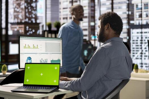 Black businessman analyzing financial data next to chroma key screen, reviewing company strategies on computer and contributing to business development and decision making. Successful forecast. photo