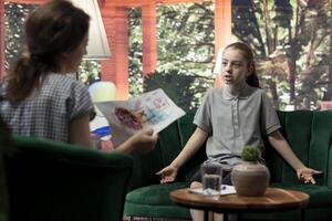 Young girl getting angry at psychologist when reviewing disturbing drawings, showing signs of murder deviant behavior. Teenager with social problems and anger management issues. photo
