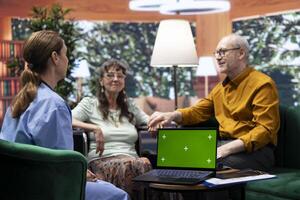 Senior woman with disability asking nurse for advice and medicine, doing consultation at home next to chroma key copy space screen. Old patients discussing about treatment for recovery. photo