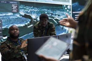 Army professionals in command post overseeing satellite data and real time surveillance, mission intelligence. Working to support strategic military operations, studying world map and big screen. photo