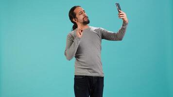 Man using smartphone to take selfies and post them on social media, studio backdrop. Vain person taking photos using phone selfie camera, isolated over studio background, camera A