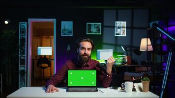 Man doing live broadcast talking to audience about recent news headlines, reading from chroma key laptop. Online show host presenting information from green screen notebook, camera B photo