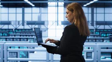 Technician doing yearly maintenance checkup using laptop to prolong data center hardware life span. IT specialist in server hub monitoring server infrastructure using notebook, camera A photo