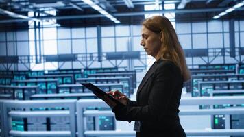 Computer scientist doing checkup, inputting data on tablet of needed fixes in server hub. Woman working in data center housing advanced data storage infrastructure supporting IT workloads, camera A photo