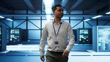 Admin walking amidst server rows, looking to ensure optimal performance and reliability by implement and managing gear. IT staff member in data center overseeing high tech facility, camera B photo