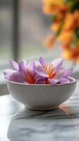 Saffron flowers in a bowl on marble table with orange flowers in background photo